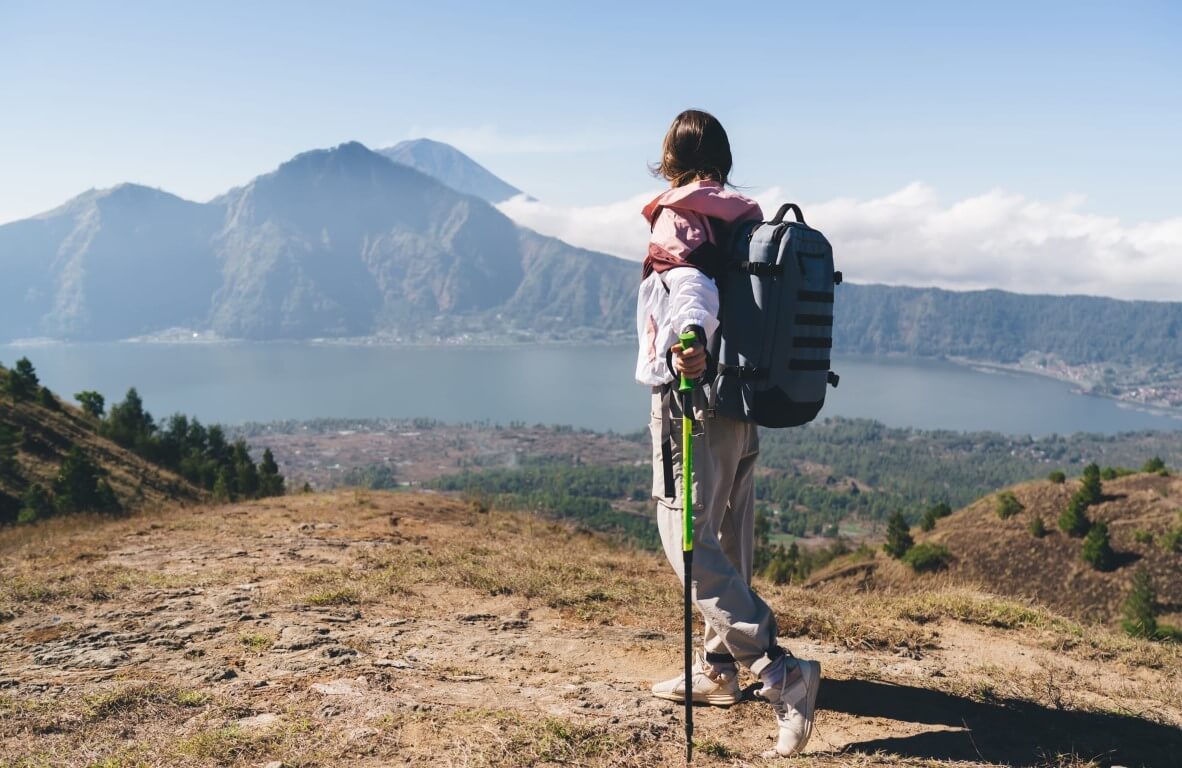 Woman with backpack standing on cliff against mountains