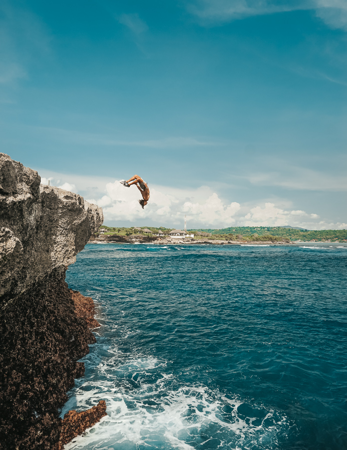 Adventurous person in mid-air, leaping off a cliff into the waters of Dream Beach