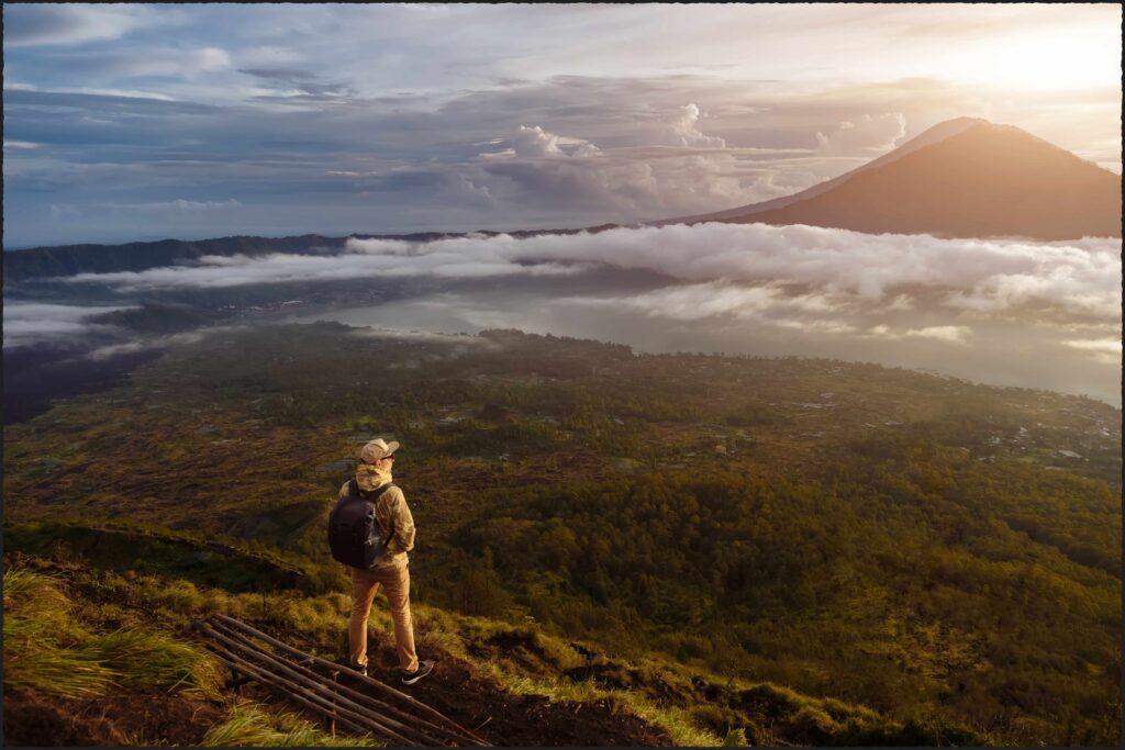 Man tourist looks at the sunrise on the volcano Batur on the island of Blai in Indonesia Hiker man with backpack travel on top volcano, travel concept