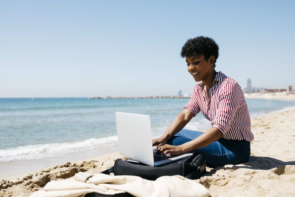 Woman sitting on the beach while working with the laptop