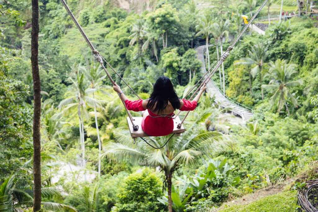 Young tourist woman swinging over the tropical rainforest at Bal