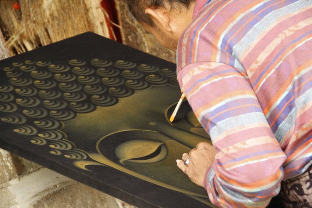 An elderly painter at The Royal Family Temple in Bali painting a Buddha Indonesia