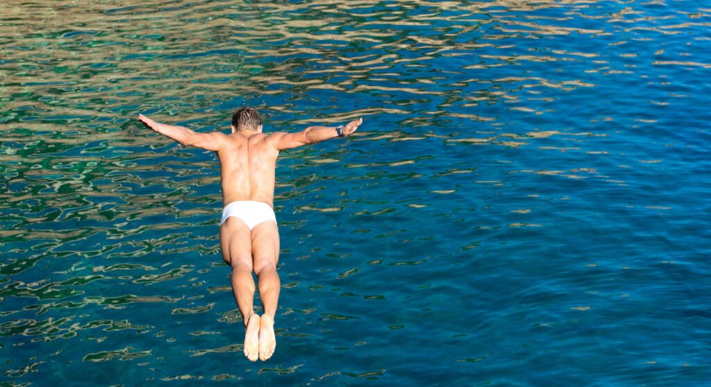 Cliff diver guy jumping in the blue sea from high rocks wall J
