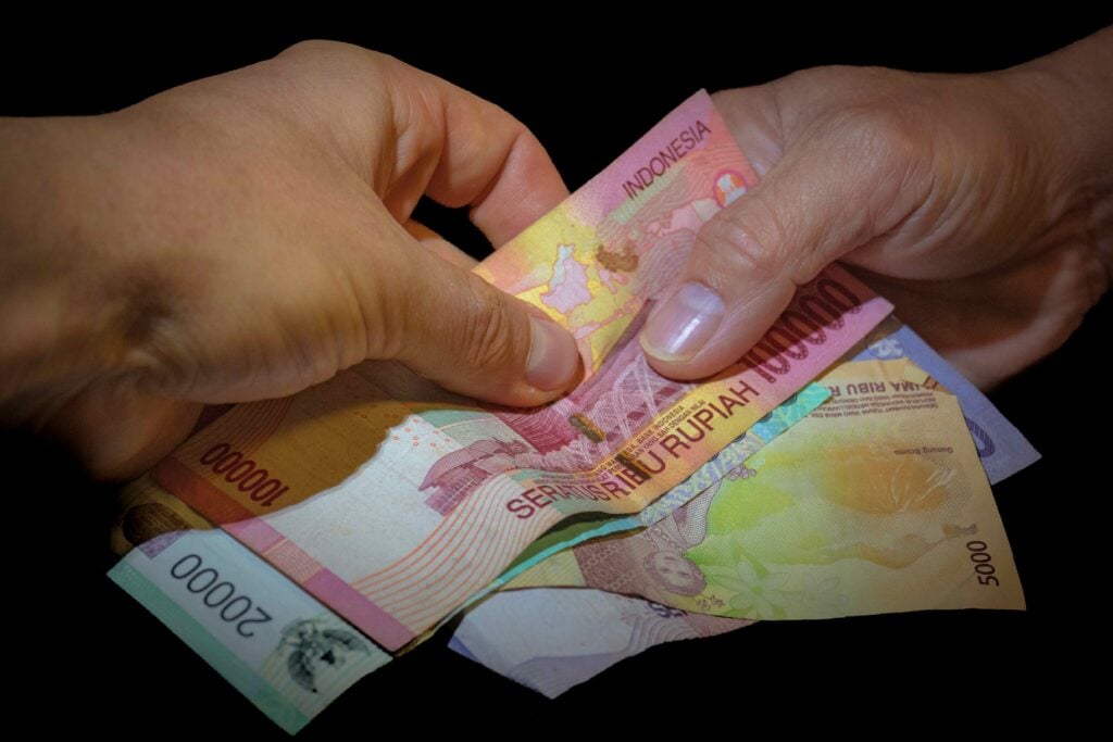 Closeup of male hands giving Indonesian Rupiah money on a dark background