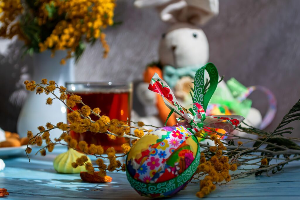 Easter composition on a blue wooden and gray background Cute bunny, colored festive egg, mimosa bouquet and hot drink in a glass