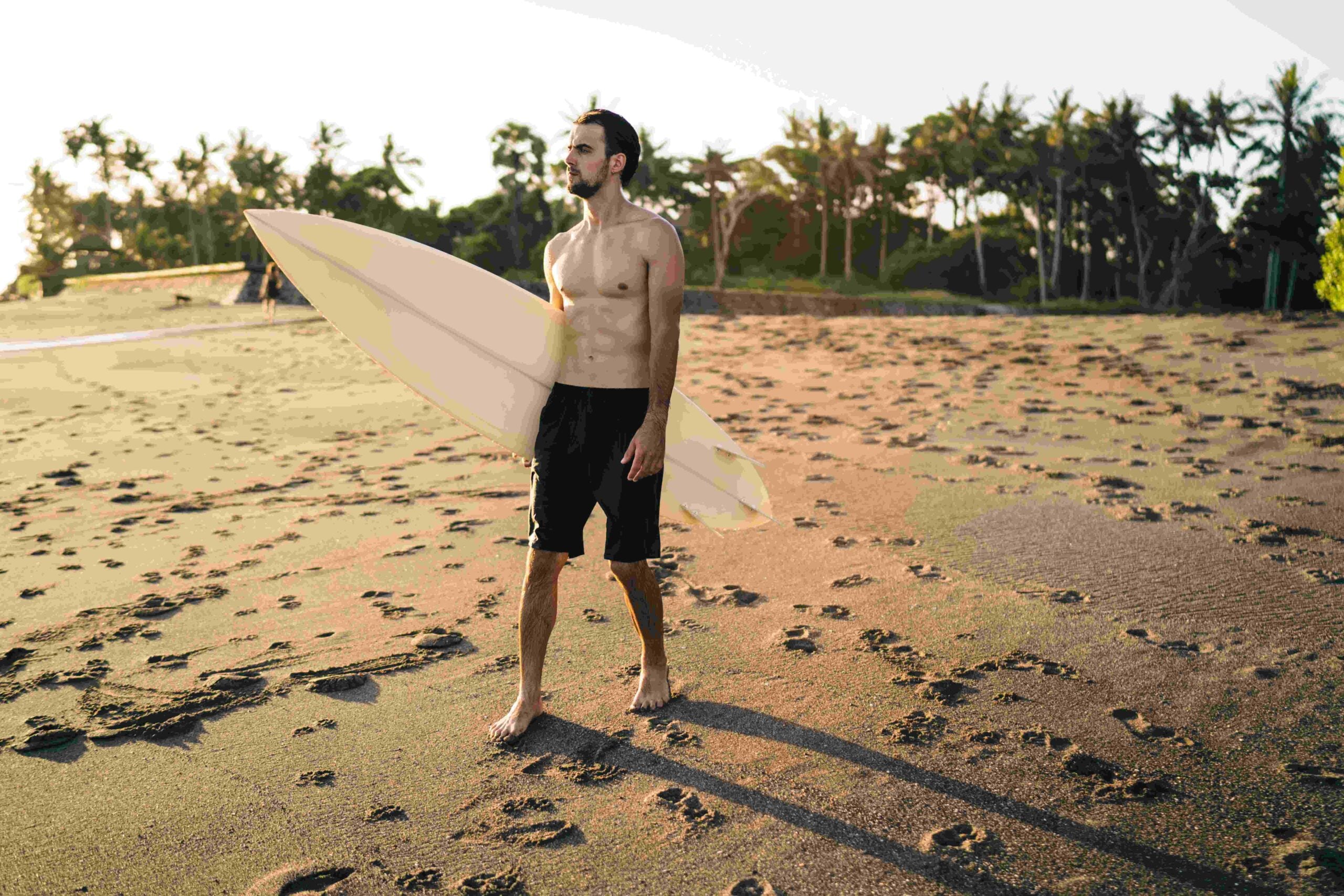 Focused young surfer standing on sand near sea and looking away