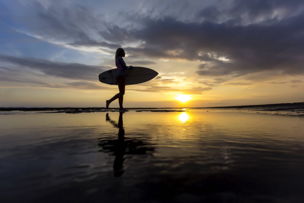 Indonesia, Bali, young woman with surfboard at sunset