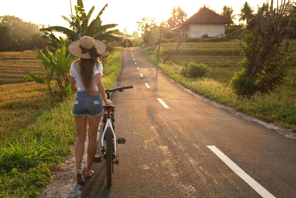 Woman is walking with a bicycle by narrow country road