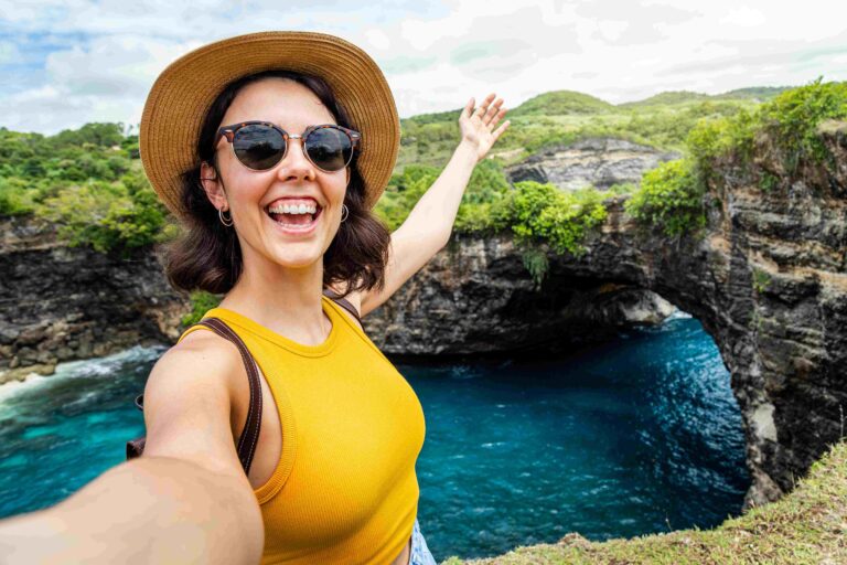 Woman with hat and sunglasses taking selfie at Broken Beach, Bali Female taking picture in summer vacation Copy space