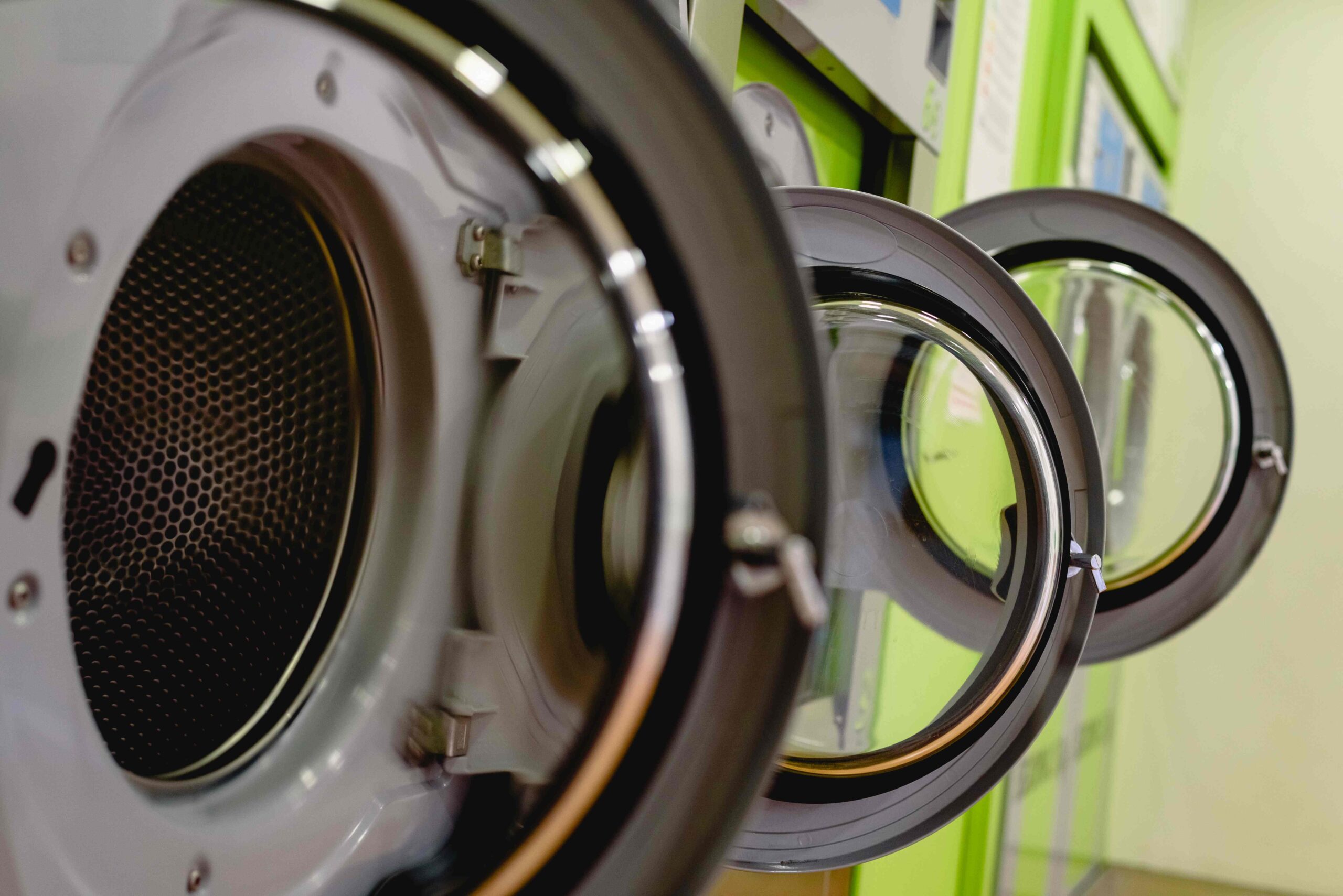 Open doors of industrial washing machines in a public laundry, d
