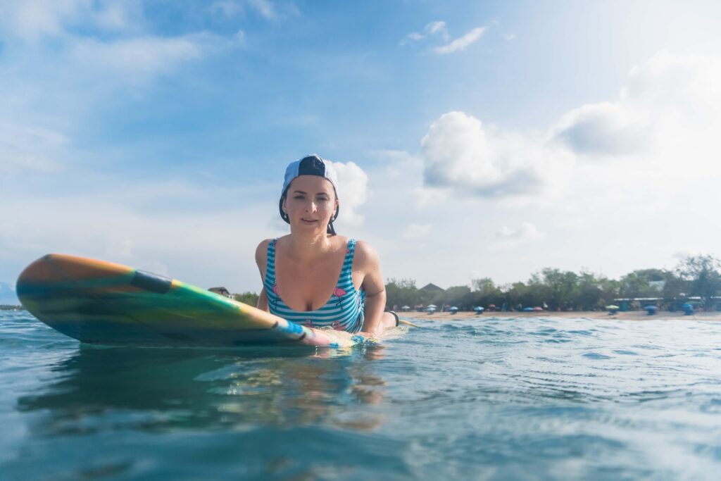 portrait of woman in swimming suit and cap lying on surfing board in ocean