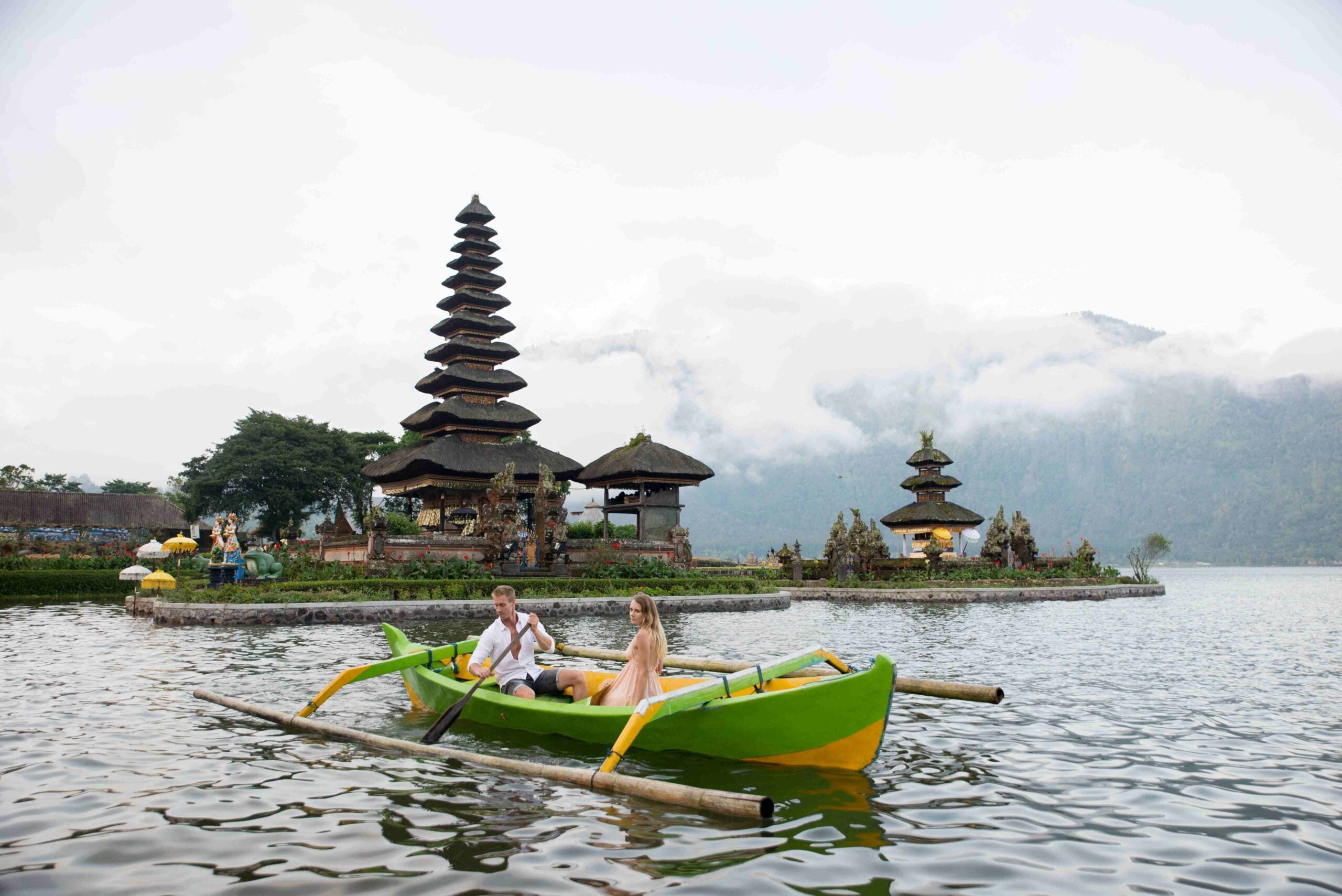 Young couple paddling on a wooden boat at Pura Ulun Danu Bratan