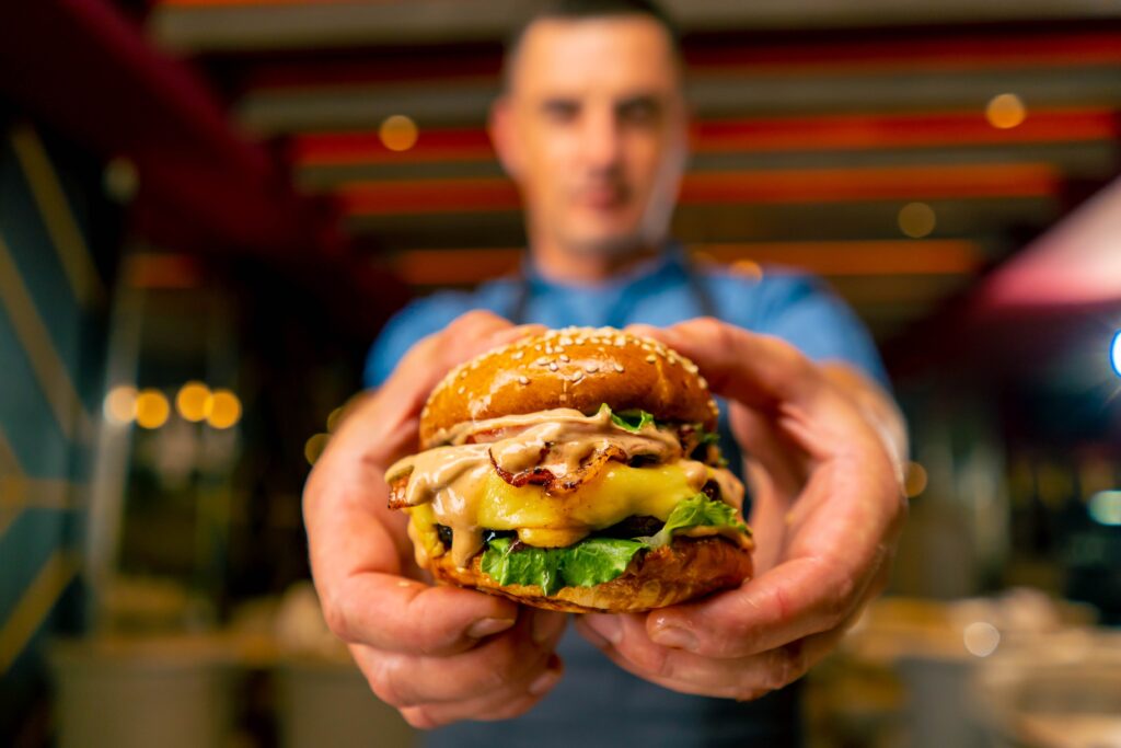 The chef of an Italian restaurant in uniform shows the burger he cooked in his professional kitchen