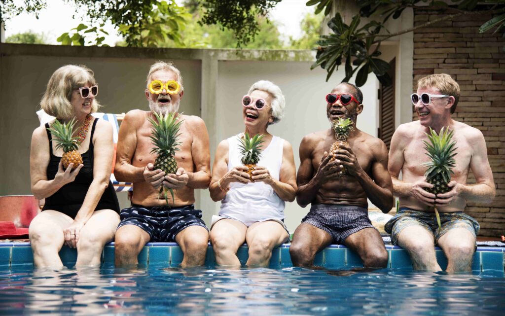 Group of diverse senior adults sitting at poolside holding pinea