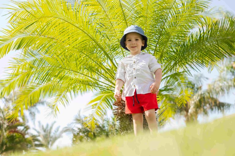 Happy little boy laying on green grass under palms