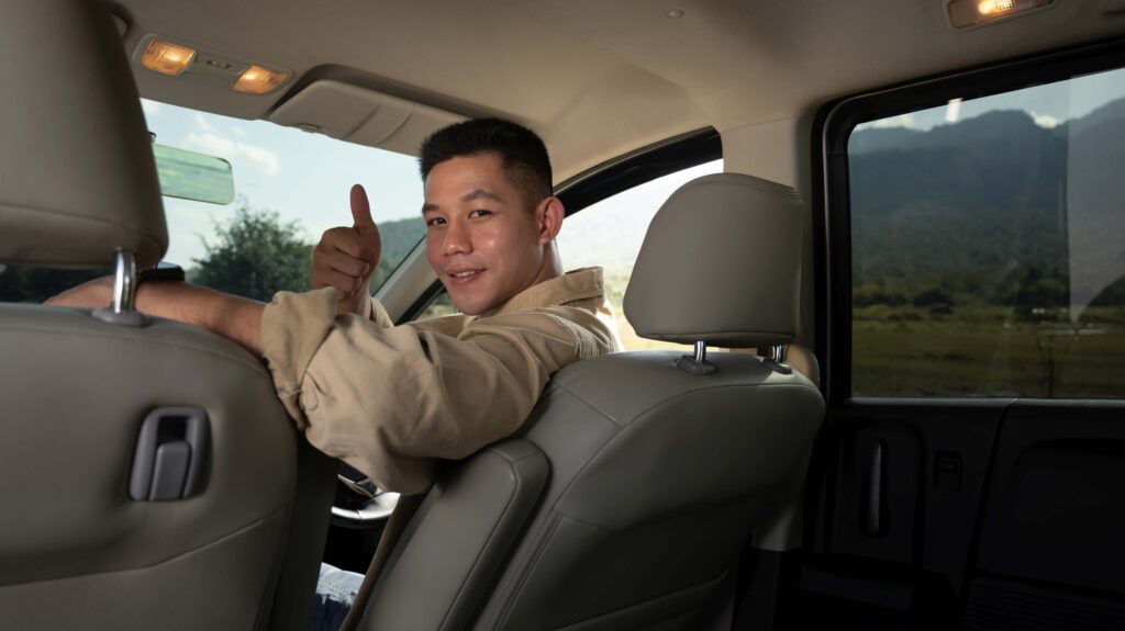 Happy young handsome man sitting inside car and showing thumbs up Travel and active lifestyle concept