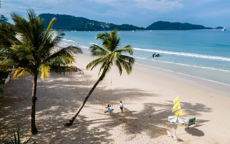 A couple of men and women on a swing under a palm tree at the beach of Patong Phuket Thailand