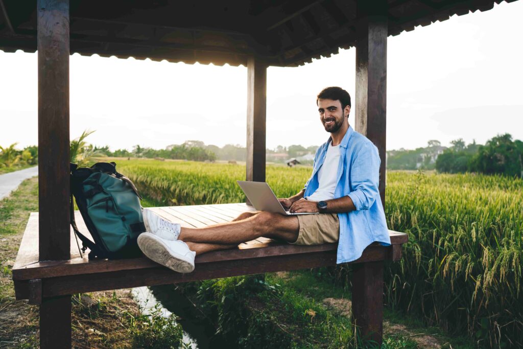 Cheerful remote worker typing on laptop in countryside pavilion