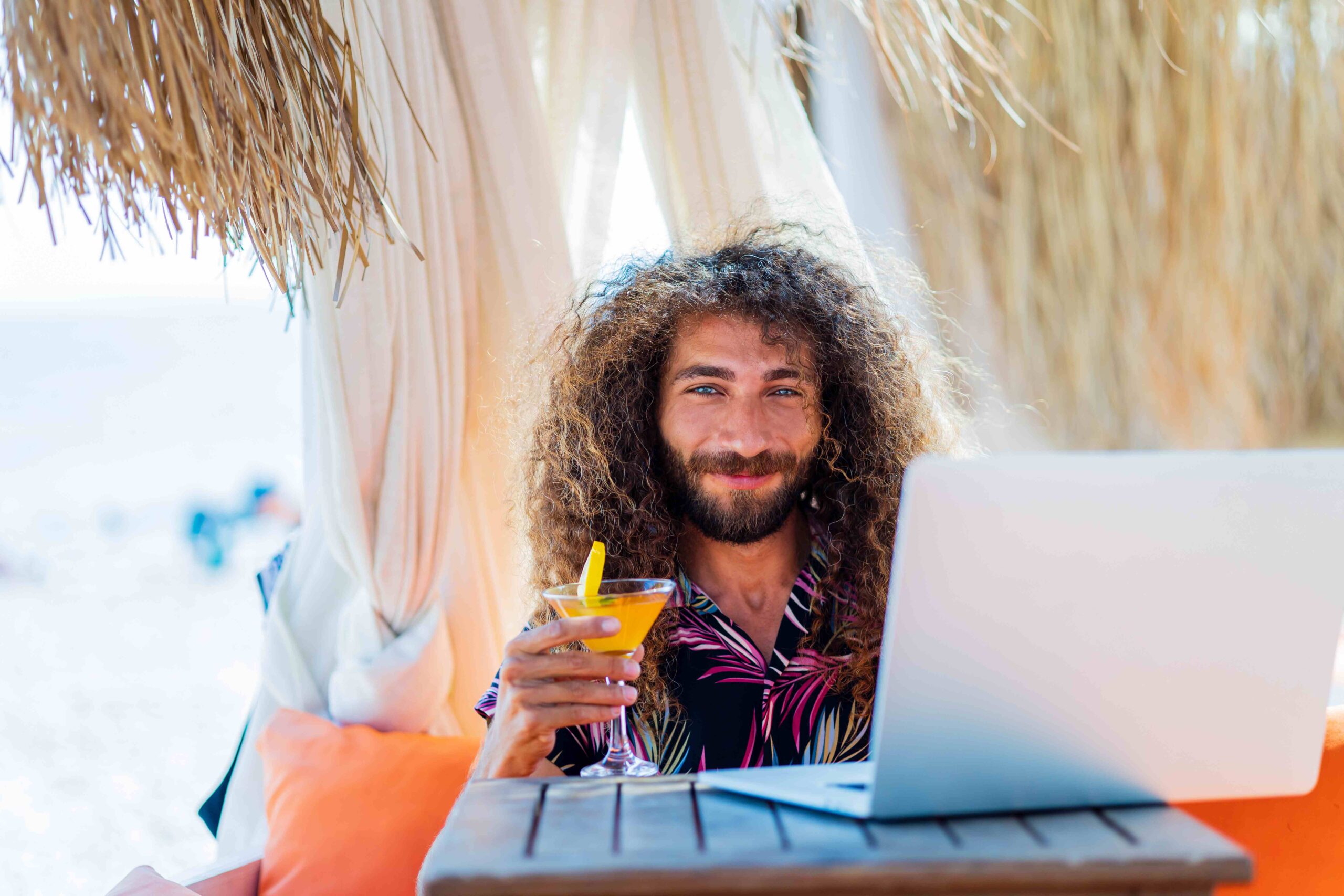 long curly haired man sitting in beach and working laptop vacation