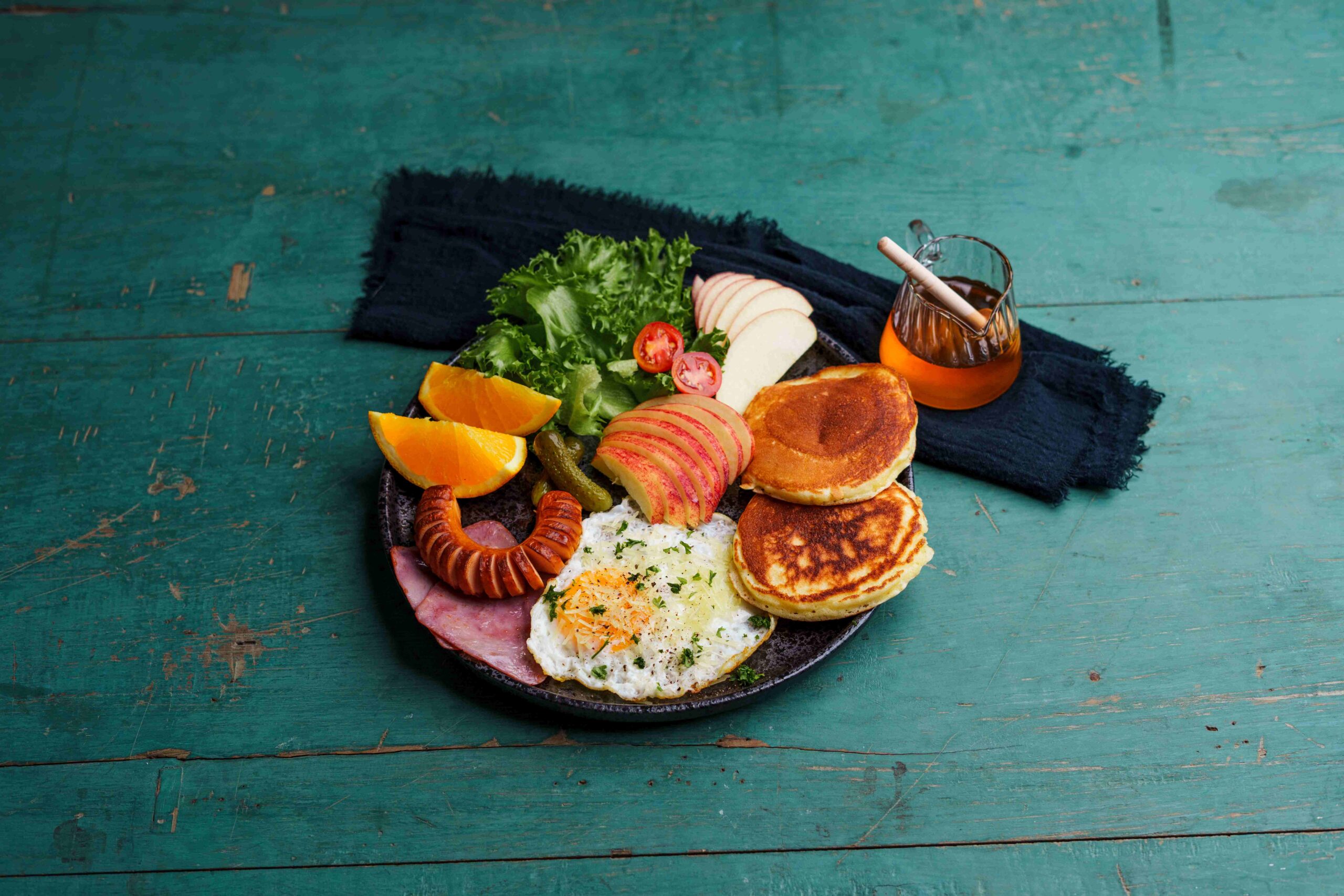 Breakfast pancakes, fried eggs, sausages, ham and fruit