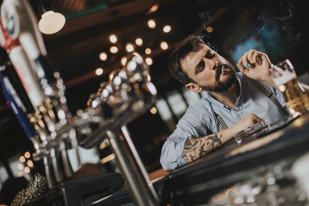 Man drinking beer and smoking cigarette at pub in the night club