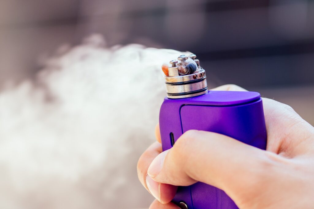 purple vape in a man's hand on a modern background