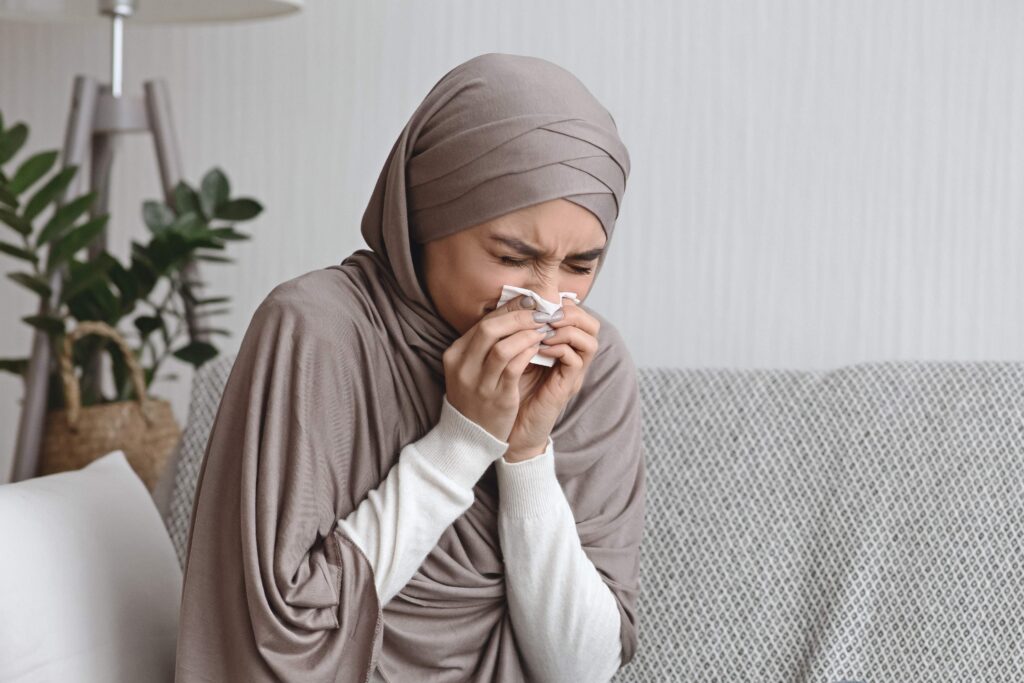 Sick muslim woman blowing runny nose to napkin at home