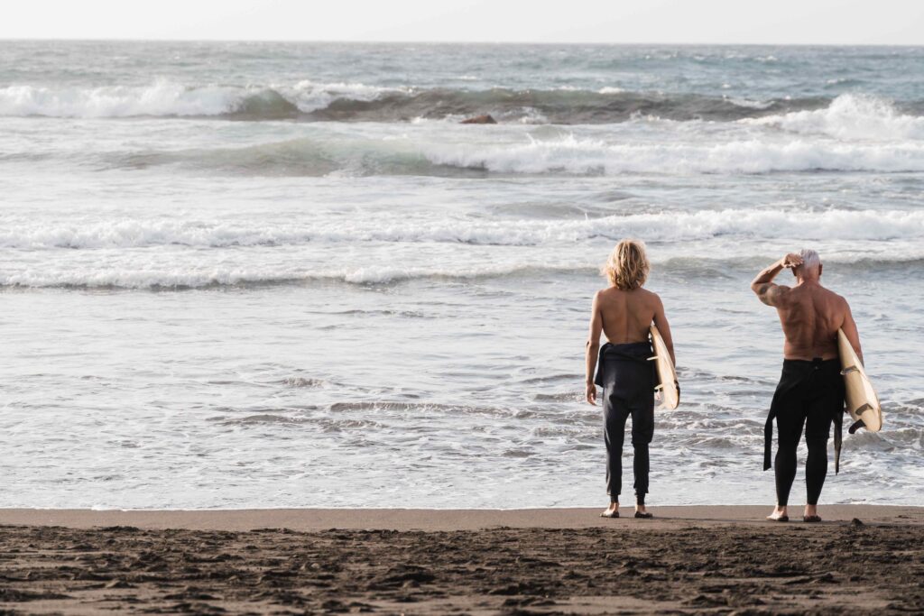 Father and son having fun on the beach at summer sunset for surf training Focus on backs