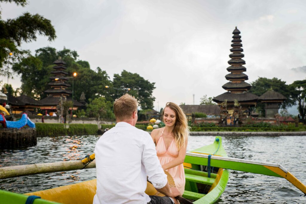 Young couple paddling on a wooden boat at Pura Ulun Danu Bratan