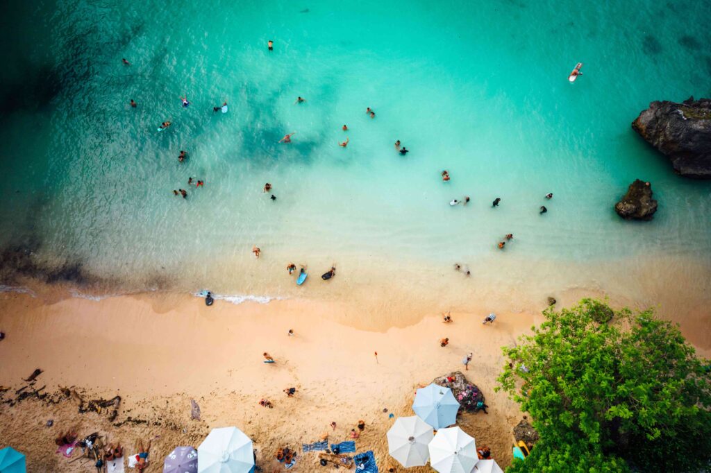 Aerial view of a paradise like bustling beach with white sand and turquoise colored waves lapping up