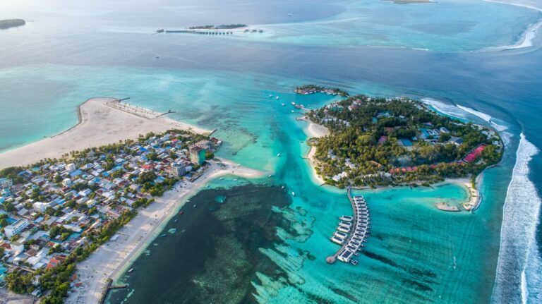 Aerial view of a tropical island with clear turquoise waters and overwater bungalows in the Maldives