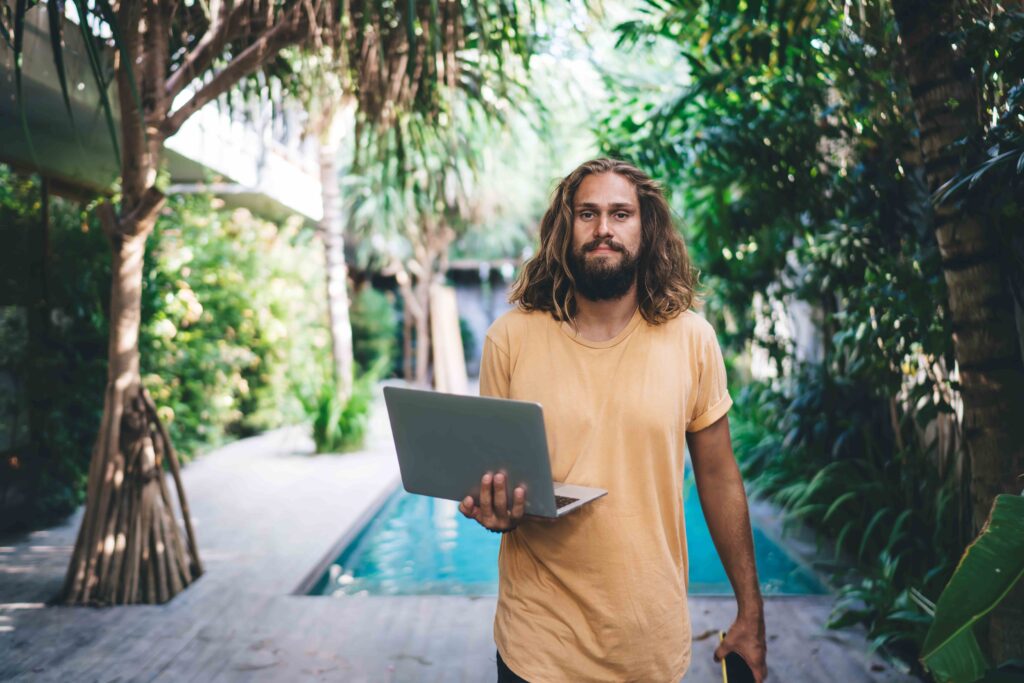 Bearded man walking with laptop near swimming pool