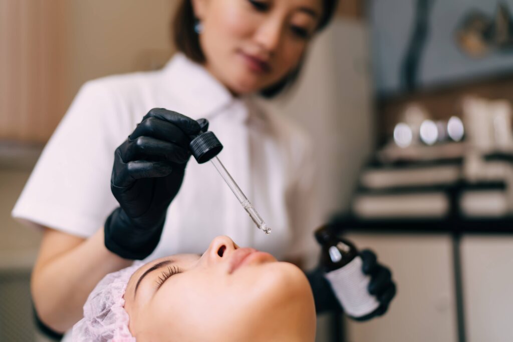 Beautician dripping oil with dropper on girl face