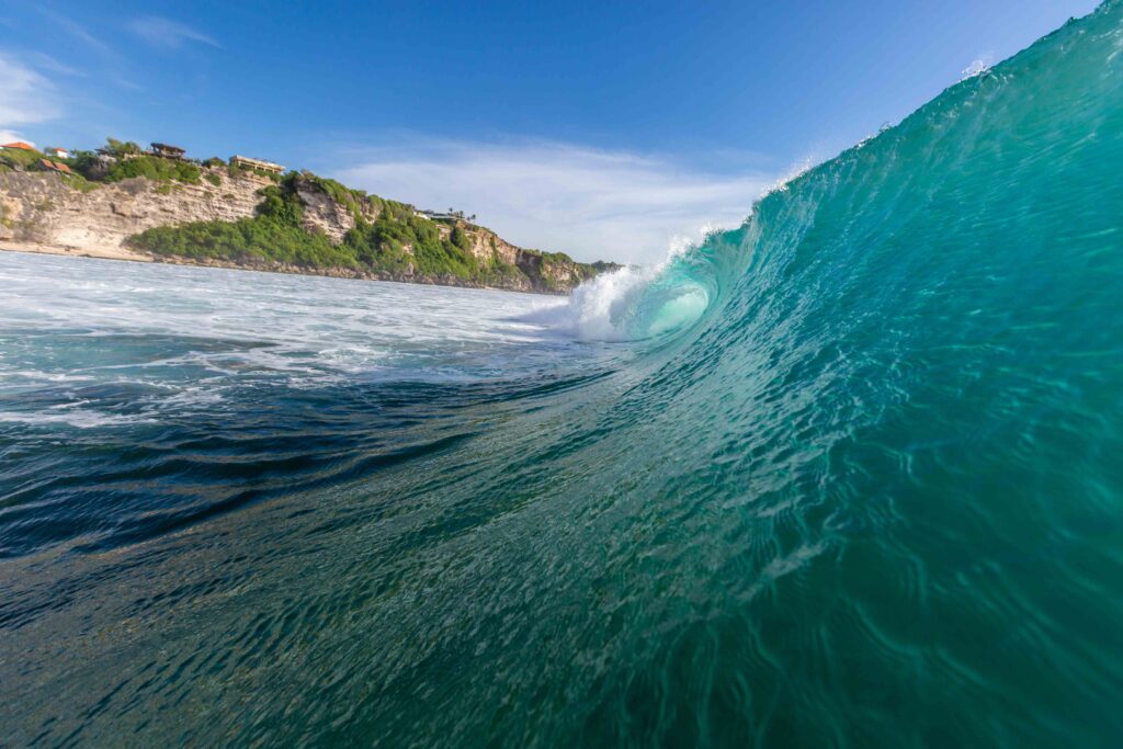 Closeup of a sea wave surrounded by mountains and greenery under a blue sky in Uluwatu in Bali