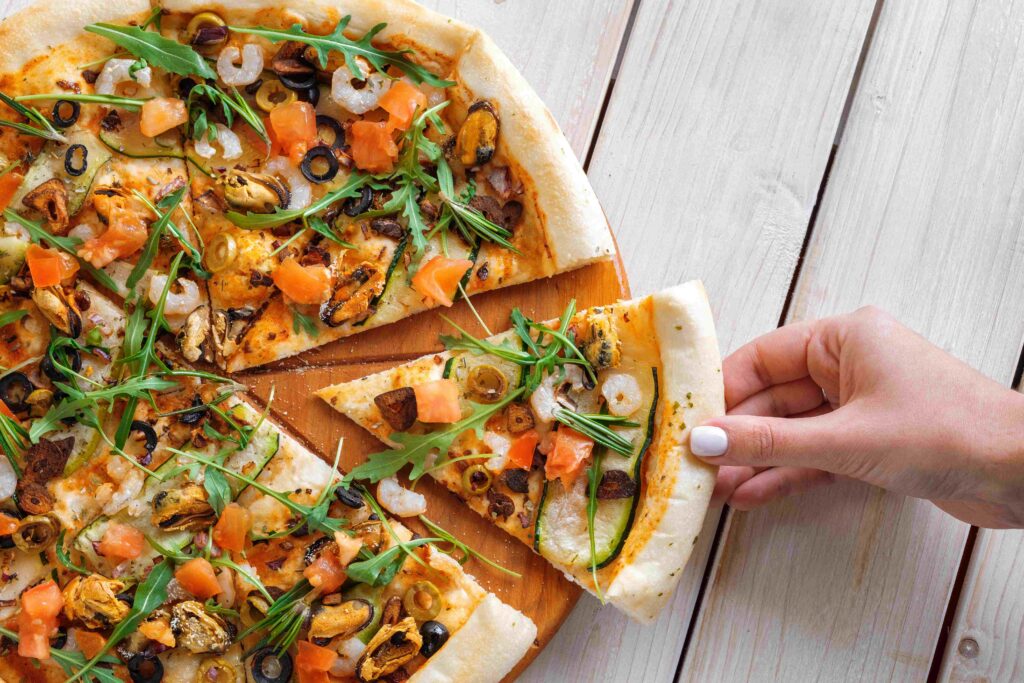 Hand picking slice of pizza with shrimps, mussels and salmon