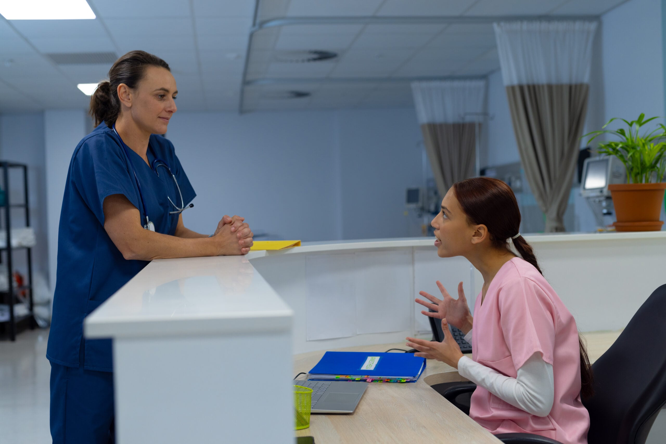Happy diverse female doctors wearing scrubs talking at reception desk at hospital Hospital, teamwork, medicine, healthcare and work, unaltered
