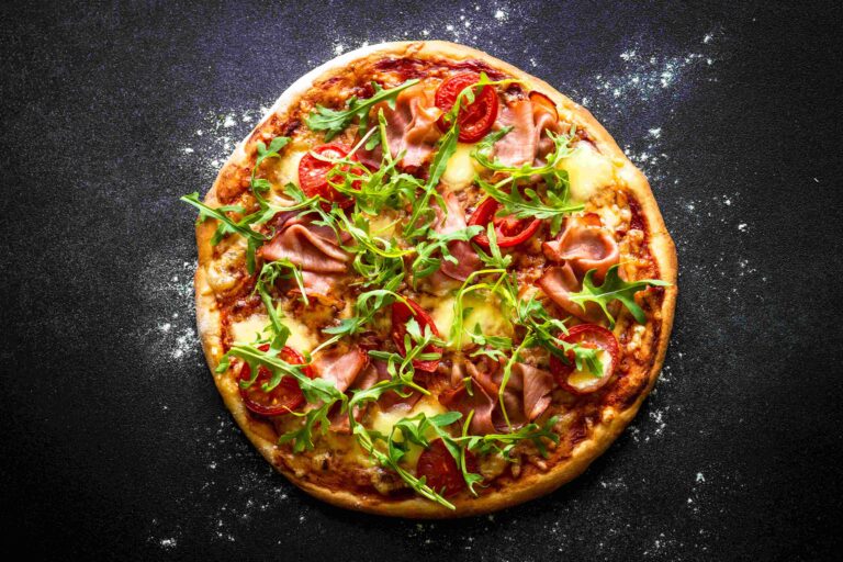 Traditional italian pizza with ham, cheese, tomatoes and arugula