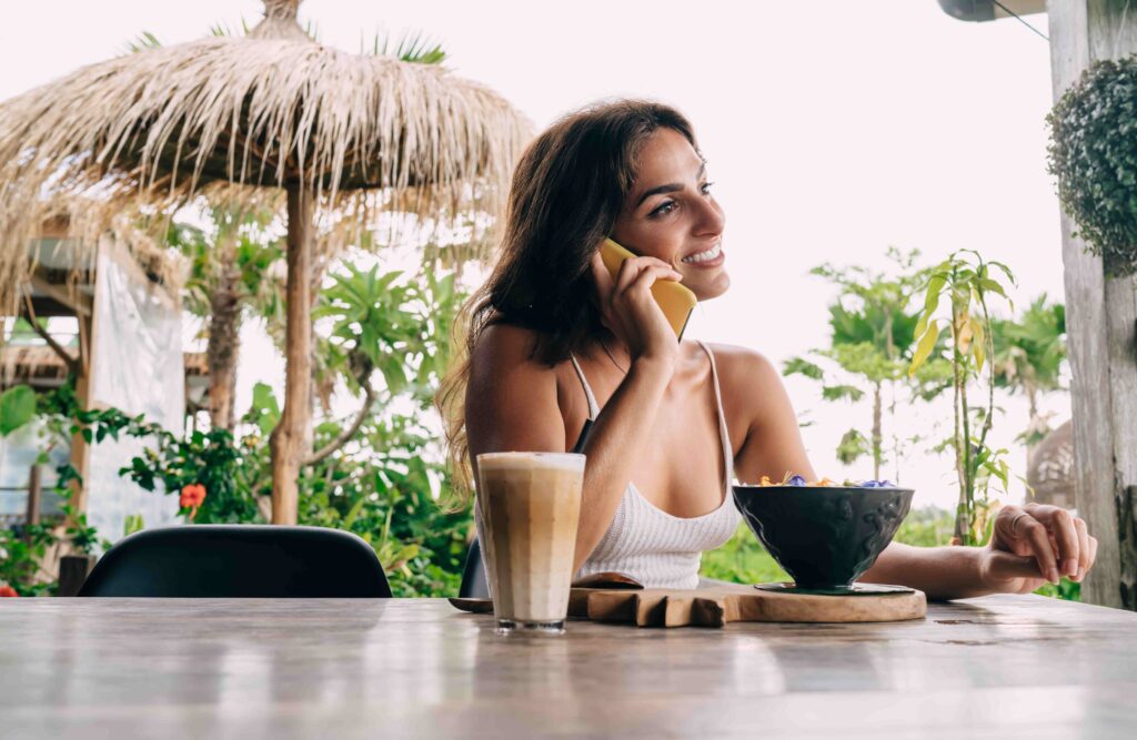 Smiling woman talking on smartphone in tropical outdoor restaurant