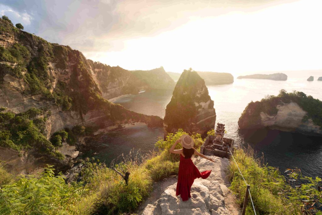 Young woman traveler enjoying and looking beautiful sunrise at Thousand island viewpoint in Nusa Penida island Bali, Indonesia