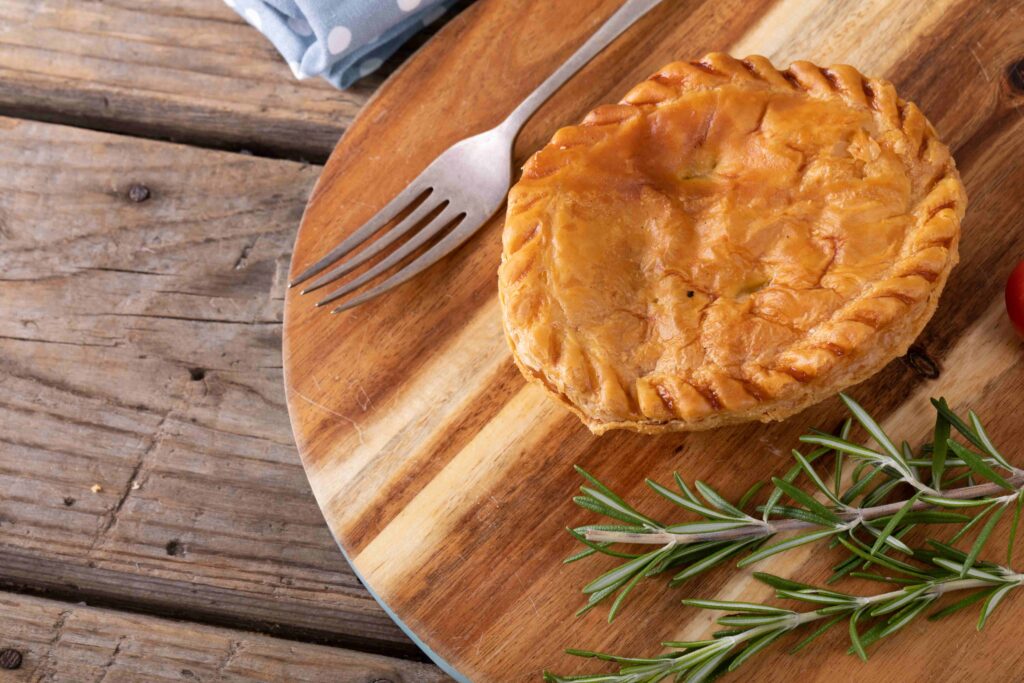 High angle view of stuffed pie with rosemary and fork on wooden serving board at table unaltered, baked and healthy food concept