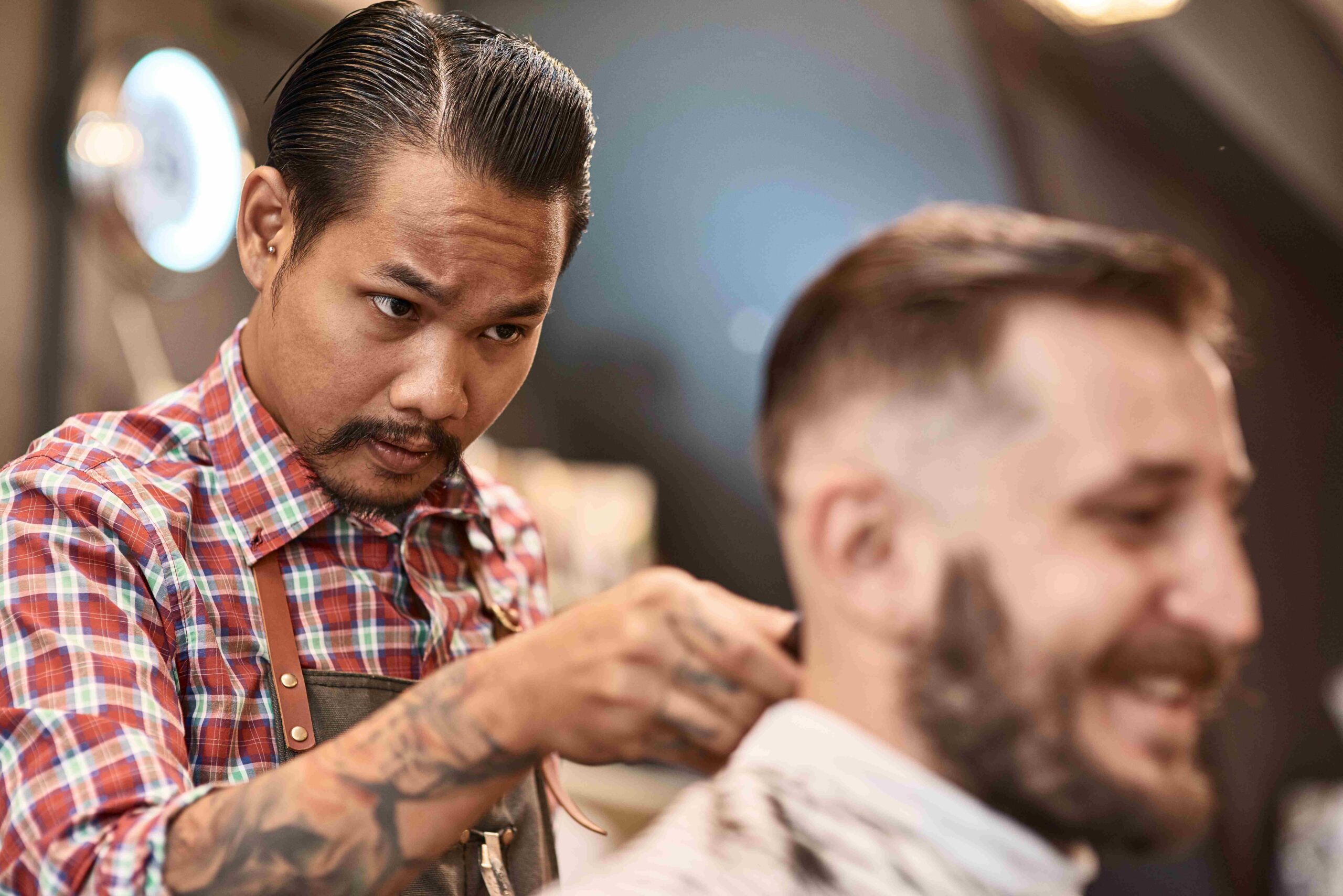 Serious professional hairdresser doing a haircut for a positive bearded man