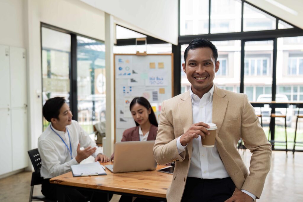 Smiling confident businessman looking at camera and standing in an office at team meeting Portrait of confident businessman with colleagues in boardroom