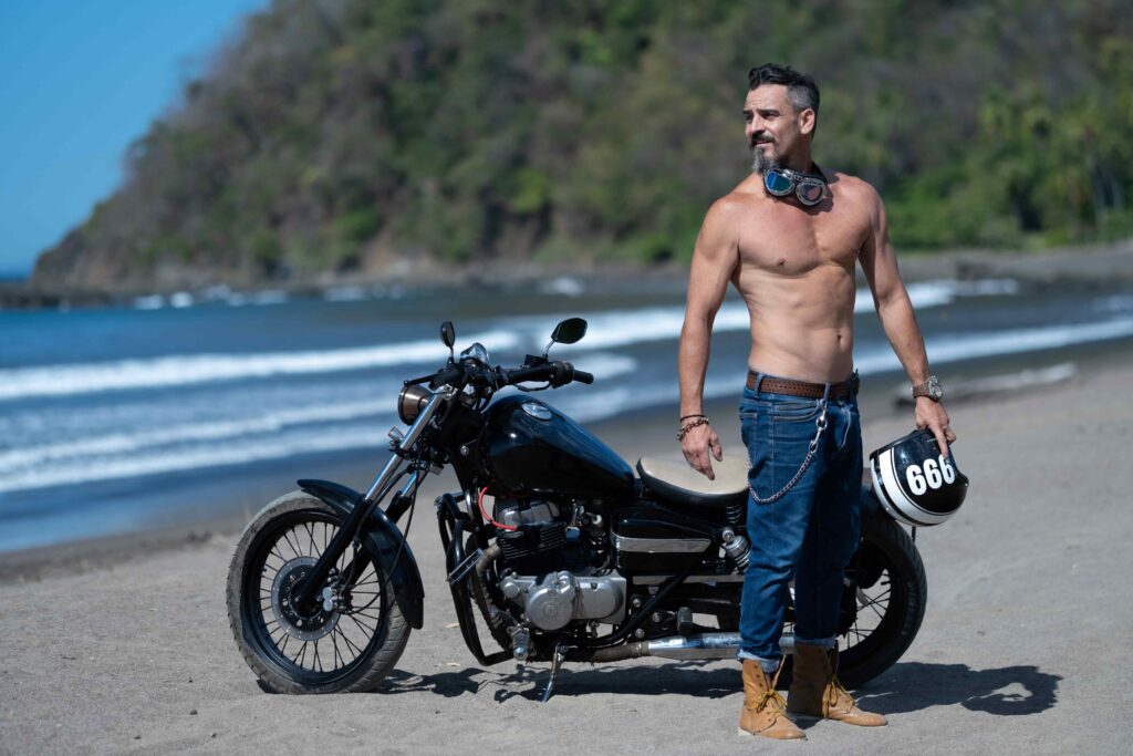 Topless male with an athletic bod beard holding a helmet while standing next to his motorbike