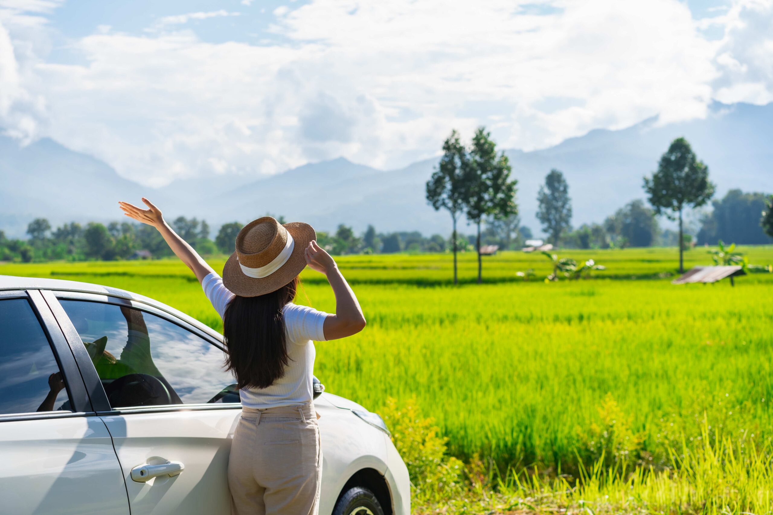 Young woman travelers with car watching a beautiful rice paddy fields and mountain view while travel driving road trip on vacation, Travel concept