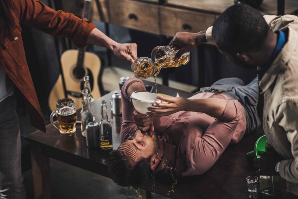 cropped shot of friends pouring beer in funnel and man drinking while lying on table