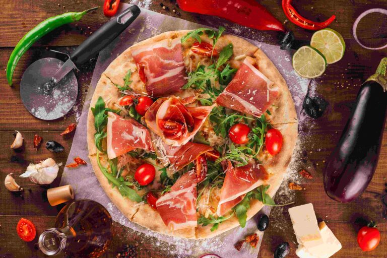 Delicious prosciutto pizza surrounded by fresh ingredients on rustic wooden table