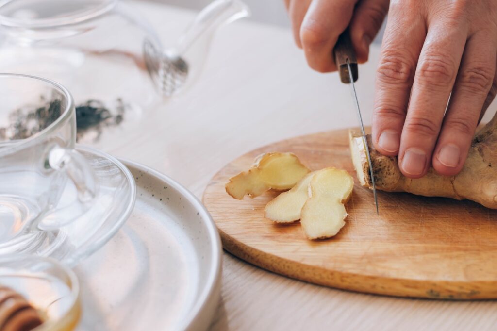 Female hands cuts fresh ginger on table Preparation of health tea, antioxidant drink