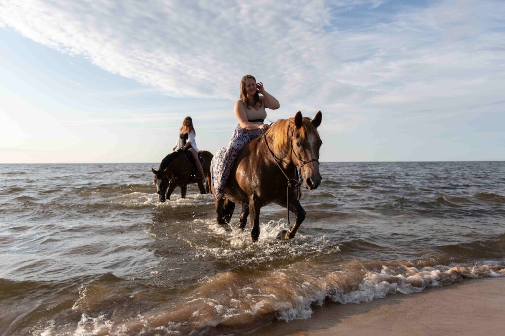 Female riders galloping on horseback through the shallow waters of a coastal beach