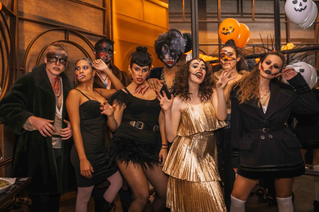 Halloween party with friends in a disco nightclub, multi ethnic group of friends sitting on a sofa in make up and costumes