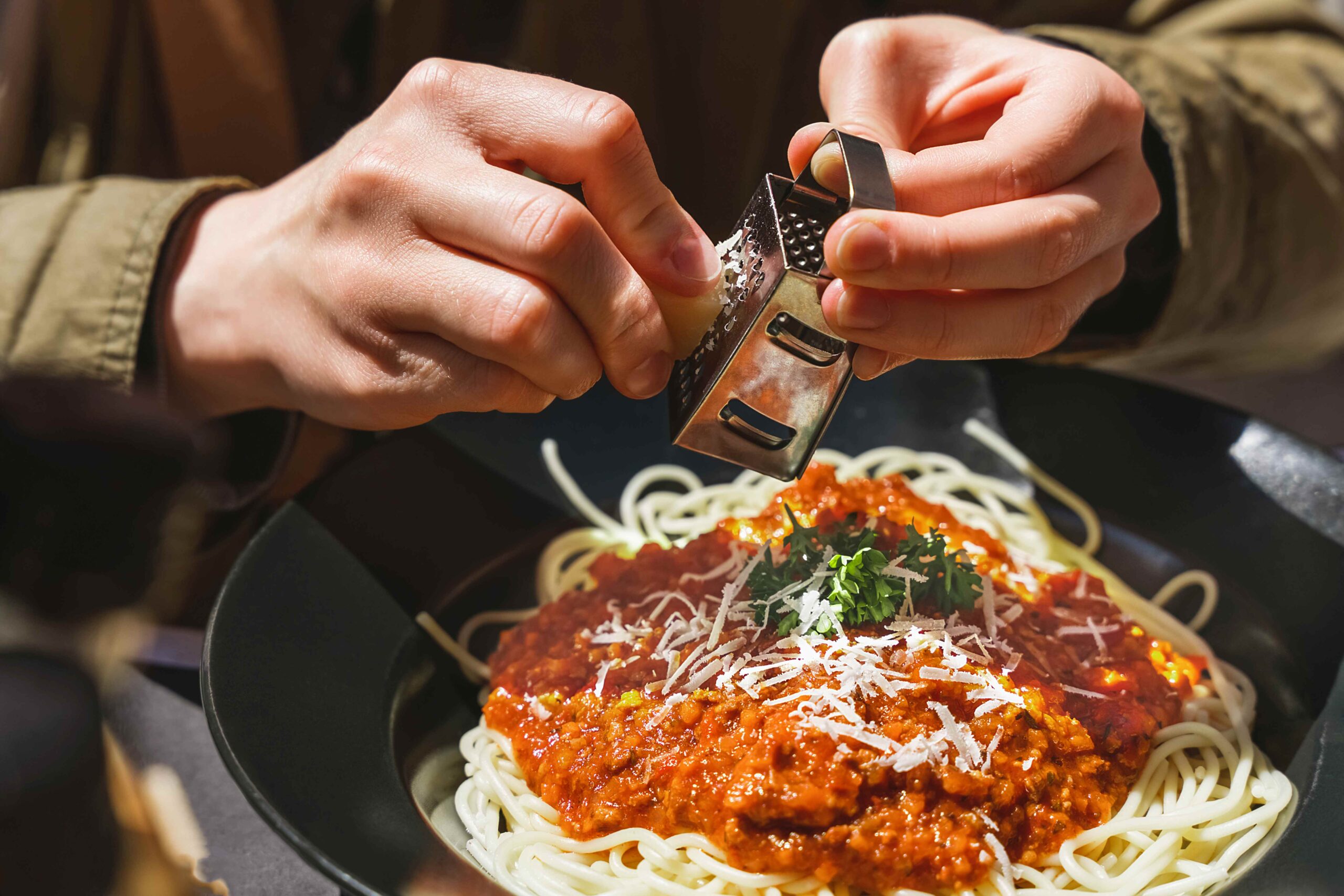 Hands grating delicious parmesan cheese on freshly made italian bolognese pasta Small box of cheese grater Italian cuisine, bolognese pasta recipe